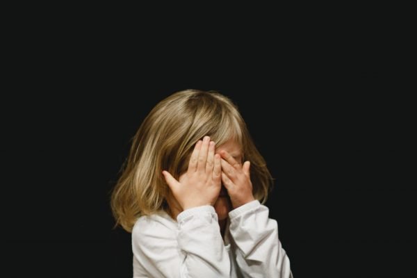 Lifestyle photography shot of little girl covering her face with her hands