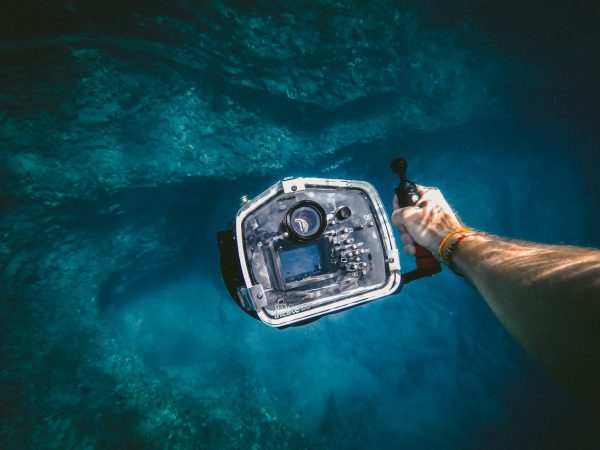image showing a man's arm holding out an underwater camera photographed under the sea