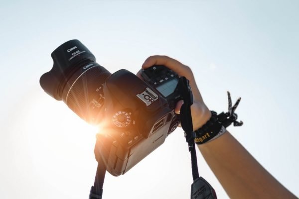 dslr camera held up in the air against the sun and blue sky